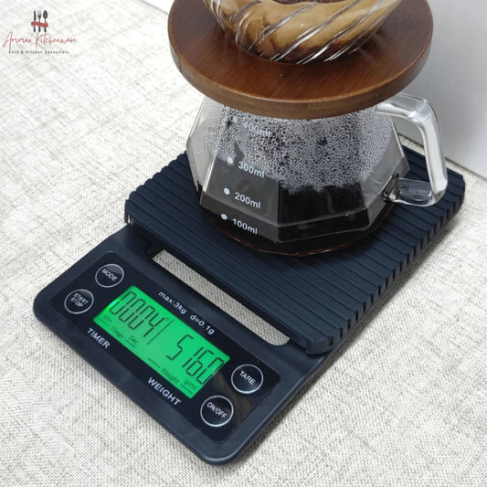 Black digital coffee scale with green dual backlit screen, integrated timer, and removable black silicone mat